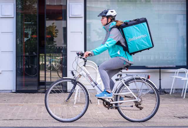 A woman on a bicycle with a large, square backpack with the Deliveroo logo.
