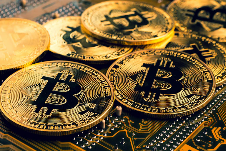A handful of gold coins with a bitcoin symbol on a mainboard