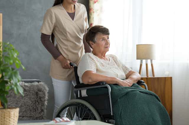 Une femme en fauteuil roulant poussé par une préposée.