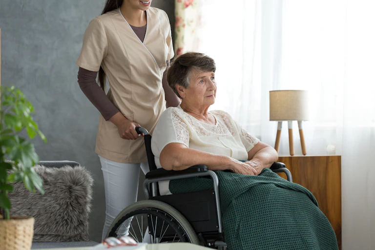 Une femme en fauteuil roulant poussé par une préposée.