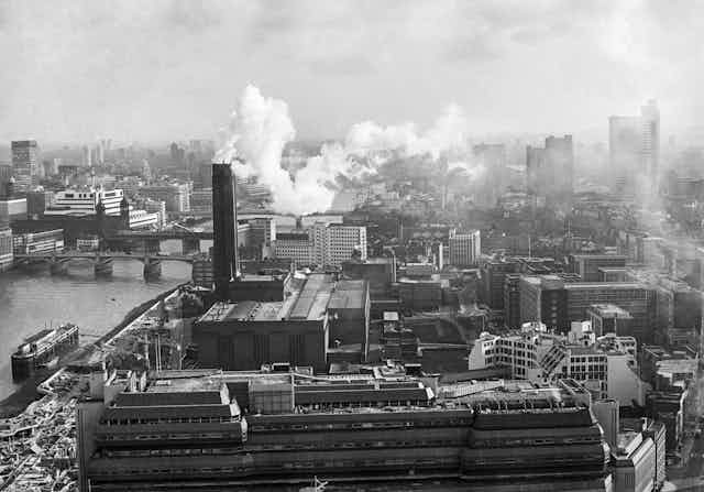 Black and white photo of power station emitting smoke in city skyline