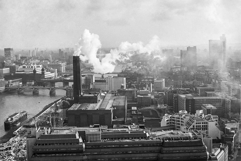 Black and white photo of power station emitting smoke in city skyline