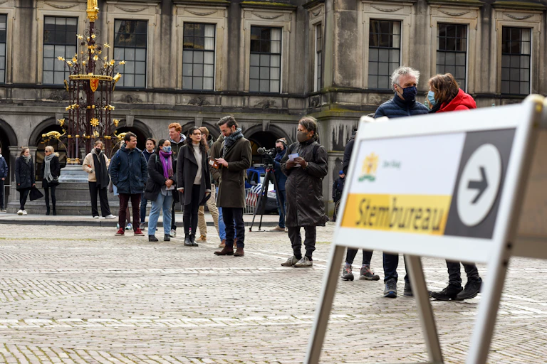 A sign read Hague polling station in English as Dutch people stand in line to vote.