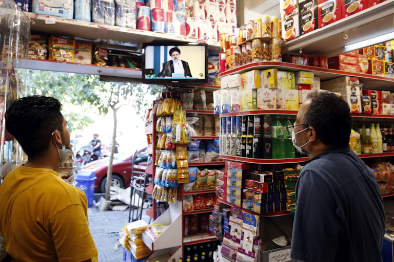 Two men in a shop watch TV presidential debate on television.