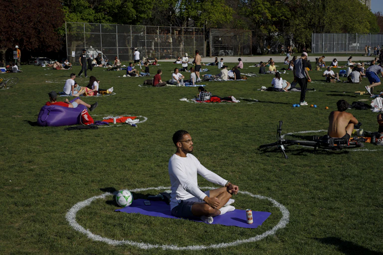 People sitting in white circles in a park. In the foreground a black man sitting on a yoga mat.