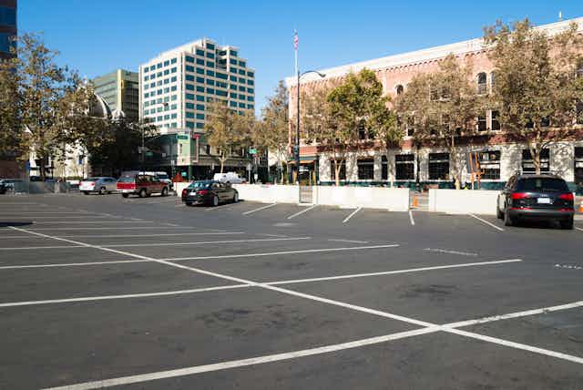 Near-empty parking lot with shops and office building in background.