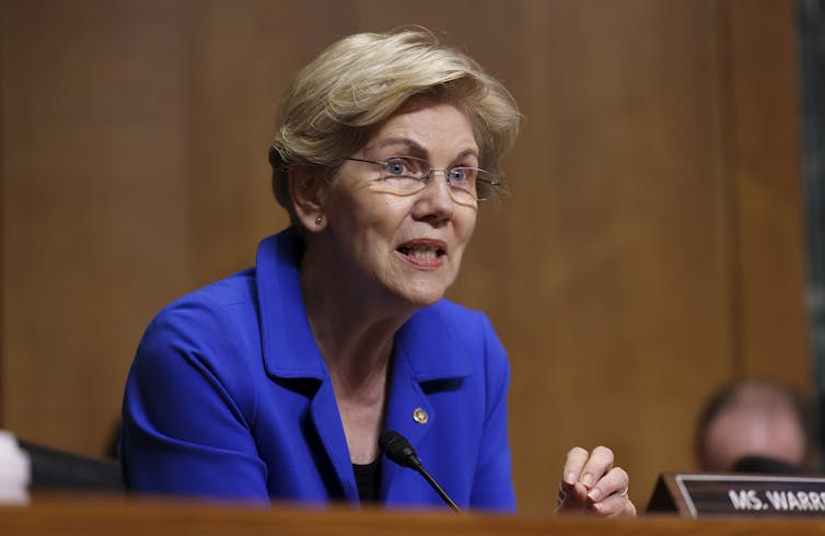Elizabeth Warren sits at a Senate committee table as she speaks