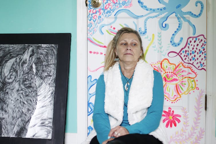 A middle-aged woman looking sad sitting in front of artwork.