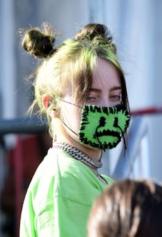Billie Eilish wears a green mask with a sad face sewed into it.