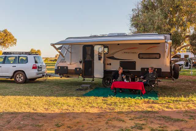 Couple sitting at table next to caravan in park