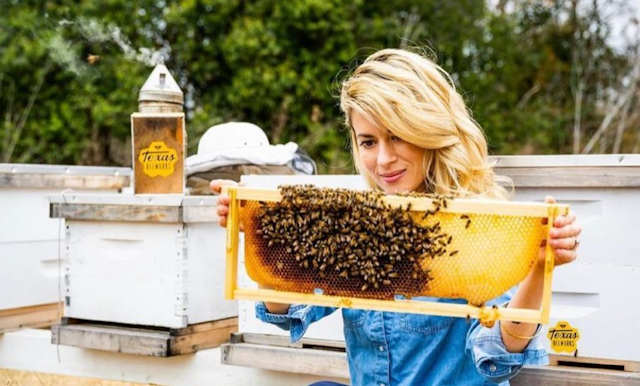 Texas Beeworks's Erika Thompson (AKA the "TikTok bee lady") holds up a honeycomb covered in bees, with no protective equipment, bare hands and free-flowing hair.