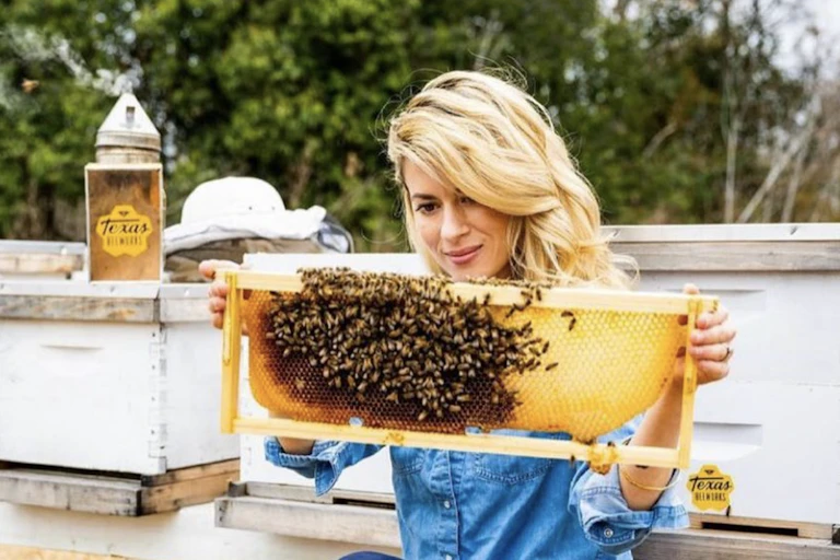Texas Beeworks's Erika Thompson (AKA the "TikTok bee lady") holds up a honeycomb covered in bees, with no protective equipment, bare hands and free-flowing hair.