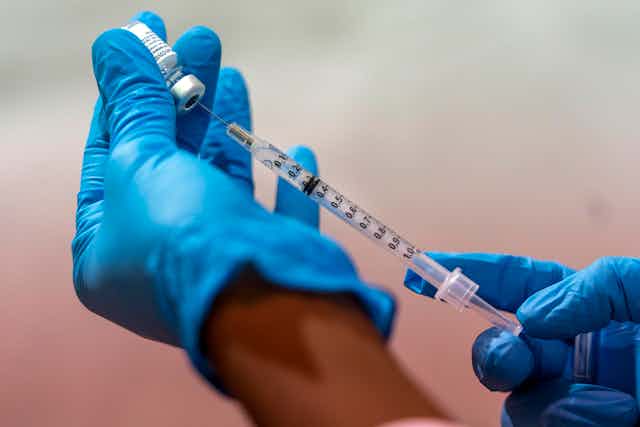 Gloved hands draw up a vaccine.