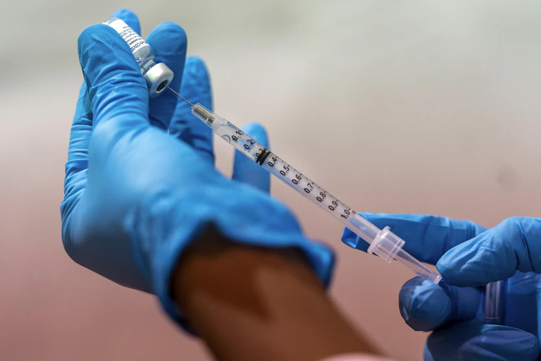 Gloved hands draw up a vaccine.