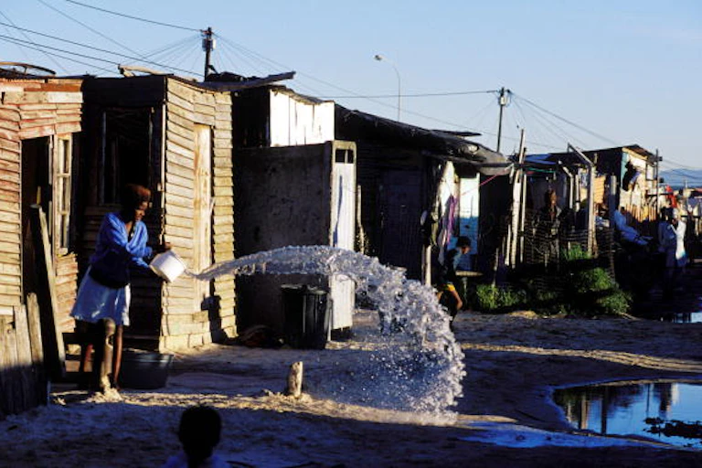 A girl throws out water from a bucket into the street in a shackland in Khayelitsha, a poor black township in Cape Town.
