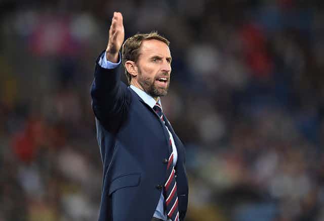 England manager Gareth Southgate wearing a blue suit and striped tie on a football pitch