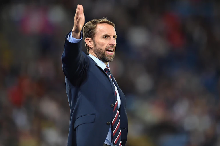 England manager Gareth Southgate wearing a blue suit and striped tie on a football pitch