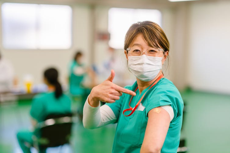 Health care worker pointing at arm after getting vaccinated.