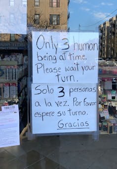 A sign in a storefront requests only three customers enter at a time.