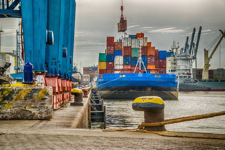 Las grúas cargan contenedores de envío en un barco atracado en el puerto.