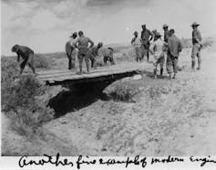 Soldiers assess a plank bridge over a gully.