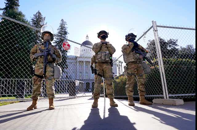 Armed soldiers stand near a fence outside the California Capitol building