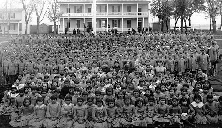Archival photo of hundreds of Native American children at a boarding school circa 1900.