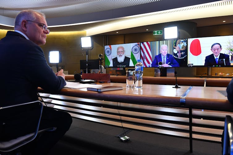 political leader in suit sits at desk in video conference with 3 others