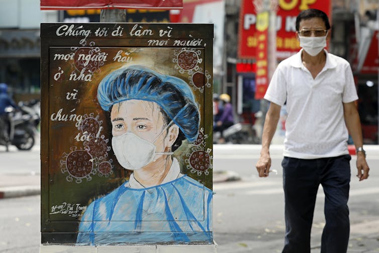 A man walks past an electrical box painted with a health-care worker.