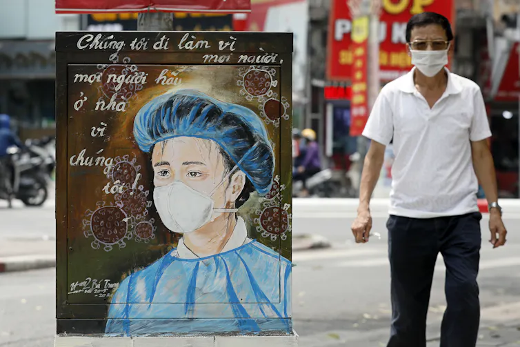 A man walks past an electrical box painted with a health-care worker.