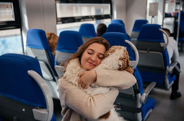 Young woman hugs her dog while travelling on a train