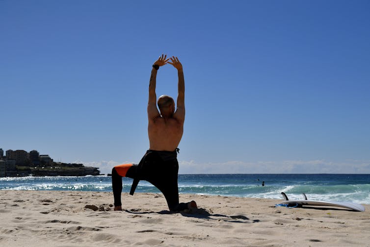 A man stretches on a beach.