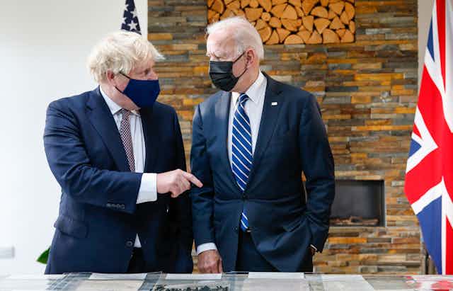 Boris Johnson and Joe Biden wearing face masks, observe the original Atlantic Charter. Johnson appears to be speaking to Biden.