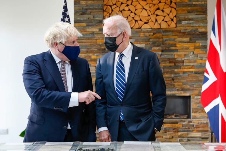 Boris Johnson and Joe Biden wearing face masks, observe the original Atlantic Charter. Johnson appears to be speaking to Biden.