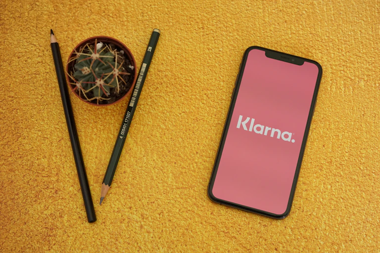 Phone with Klarna app next to a couple of pencils