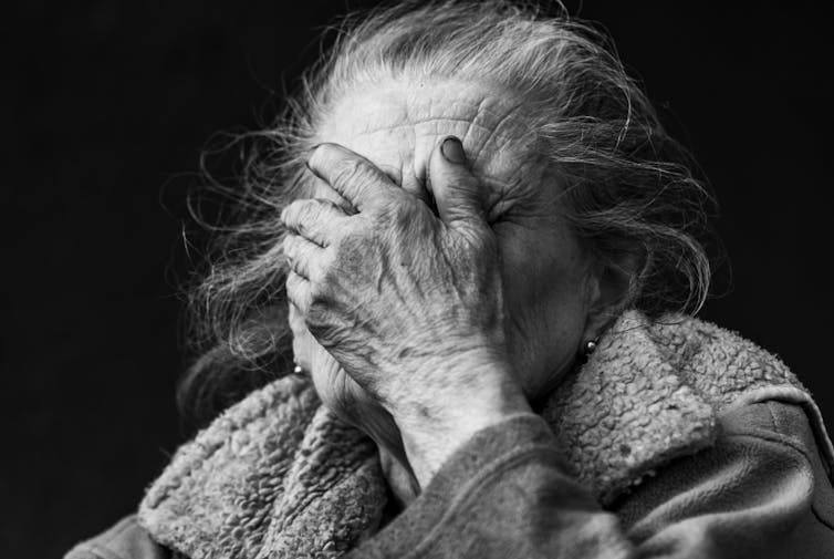 Black and white image of old lady in distress covering her face with her hand.