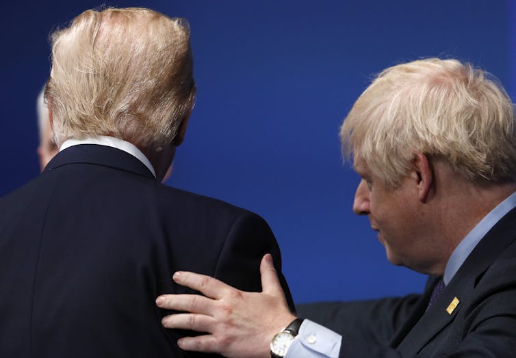 Boris Johnson places his hand on Donald Trump's back during a meeting between the two at a NATO summit. Trump is facing away from the camera.
