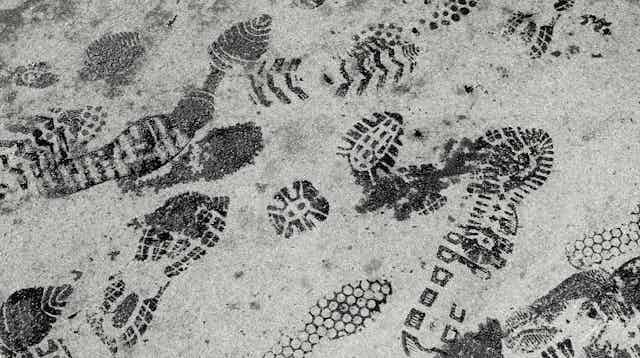 A series of dark shoe prints on a pavement.