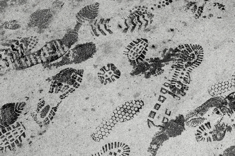 A series of dark shoe prints on a pavement.