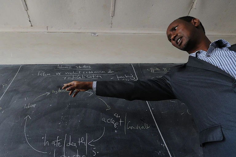 Kenyan teacher giving a lesson in front of a blackboard.