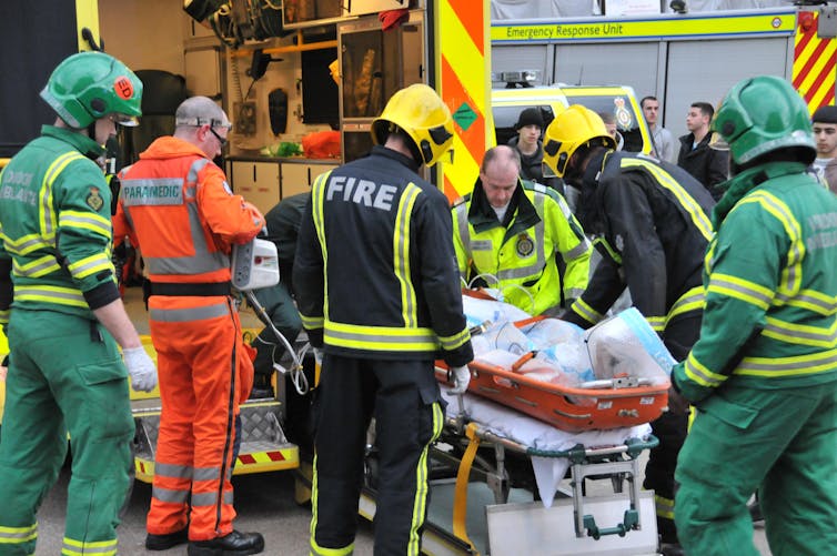Firefighters and paramedics load person on stretcher into an ambulance.
