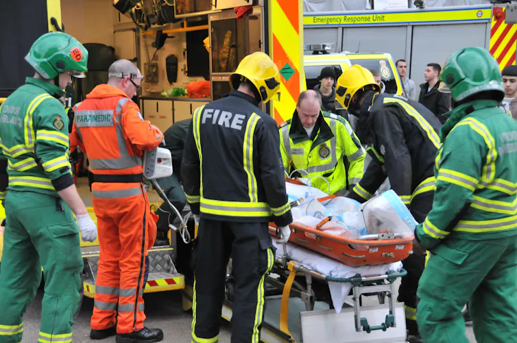 Firefighters and paramedics load person on stretcher into an ambulance.