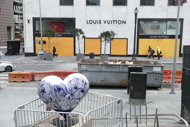 A small number of people walk past a boarded up retail shop