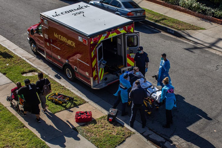 Medical workers in protective equipment load a patient into an ambulance