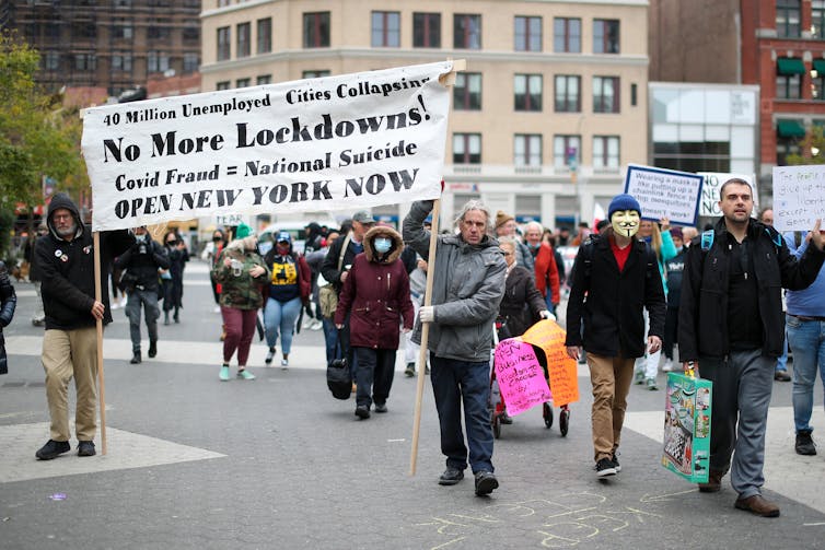 A group of people walk down a street holding a sign calling for an end to lockdowns