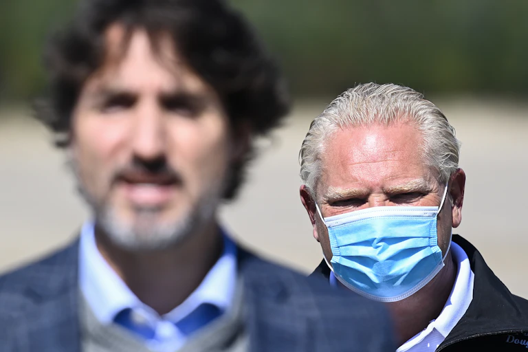 Doug Ford, wearing a mask, is seen behind Justin Trudeau.