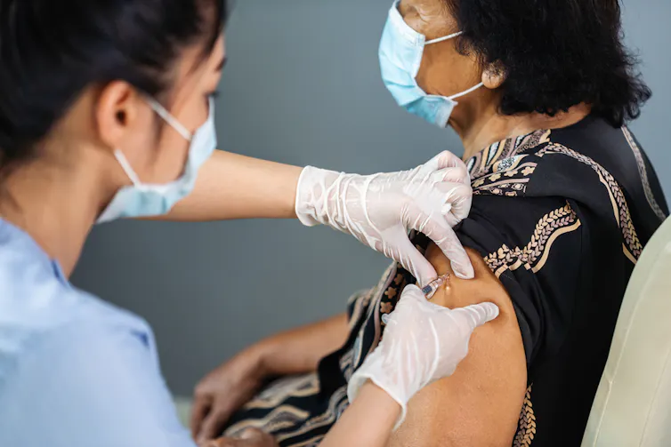 Médica aplicando a una anciana india una vacuna en el hombro