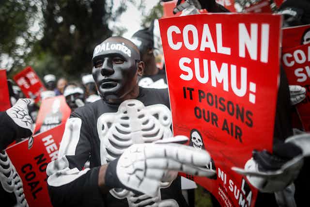 Man in skeleton outfit holds sign saying 'Coal ni sumu'
