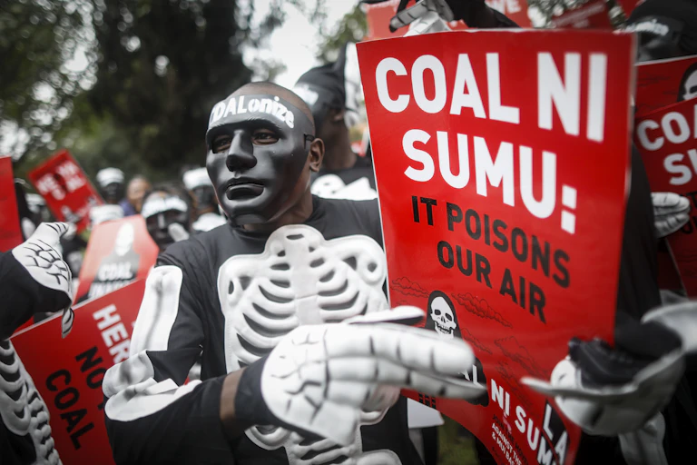 Man in skeleton outfit holds sign saying 'Coal ni sumu'