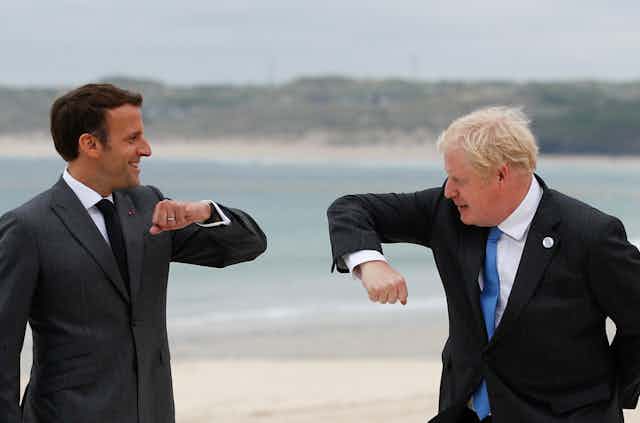 French President Emmanuel Macron and British Prime Minister Boris Johnson hold out their arms with their elbows pointing toward each other as they prepare for an elbow bump during a G-7 meeting